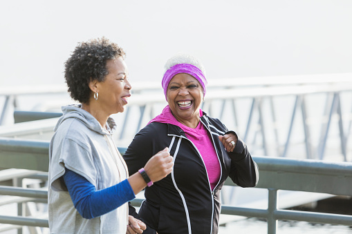 Two African-American women exercising together, jogging or power walking side by side. The senior woman with white hair is in her 60s. Her friend is in her 50s.