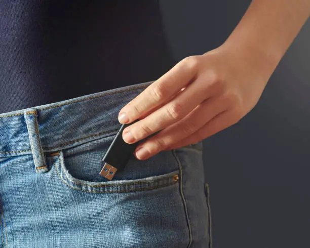 Photo of Young woman pushing usb flash drive into a jeans pocket