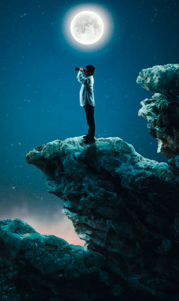 istock Kid on top of a cliff looking with binocular in the night. 920534408
