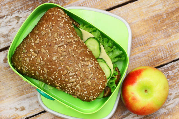 istock Brown cheese roll with cucumber and lettuce in lunch box and red apple 920539112