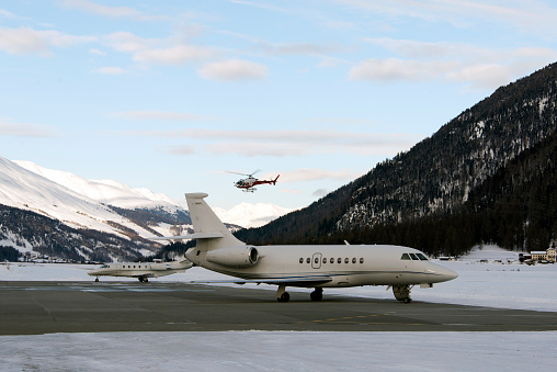 A red helicopter flying over two private jets in the airport of St Moritz Switzerland IN WINTER