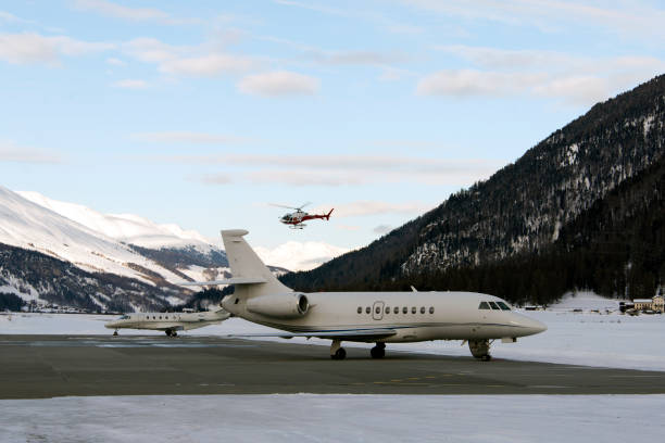 A red helicopter flying over two private jets in the airport of St Moritz Switzerland IN WINTER A red helicopter flying over two private jets in the airport of St Moritz Switzerland IN WINTER samedan stock pictures, royalty-free photos & images