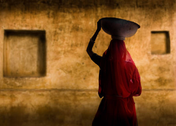 A picture of an Indian woman in a red dress An Indian woman carrying on with her work. silhouette of the indian girls in saree stock pictures, royalty-free photos & images