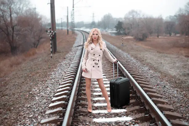 Blondewoman waiting at the railway with a suitcase.