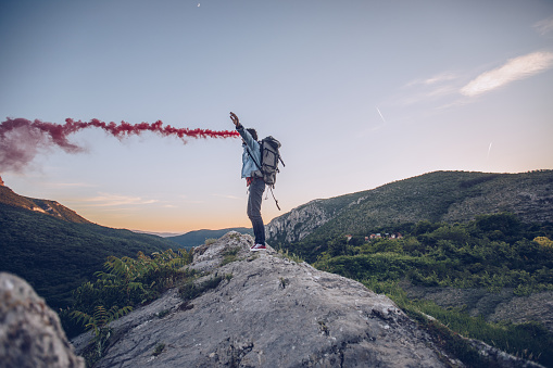 Hiker with open arms holds a signal smoke flare