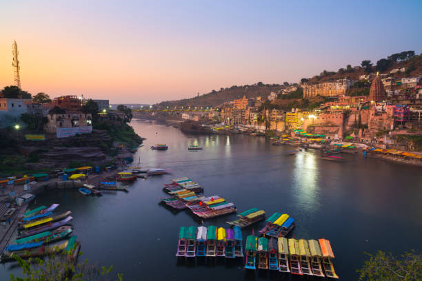 paesaggio urbano di omkareshwar al crepuscolo, india, tempio sacro indù. fiume narmada sacro, barche galleggianti. meta di viaggio per turisti e pellegrini. - shiva india hinduism temple foto e immagini stock