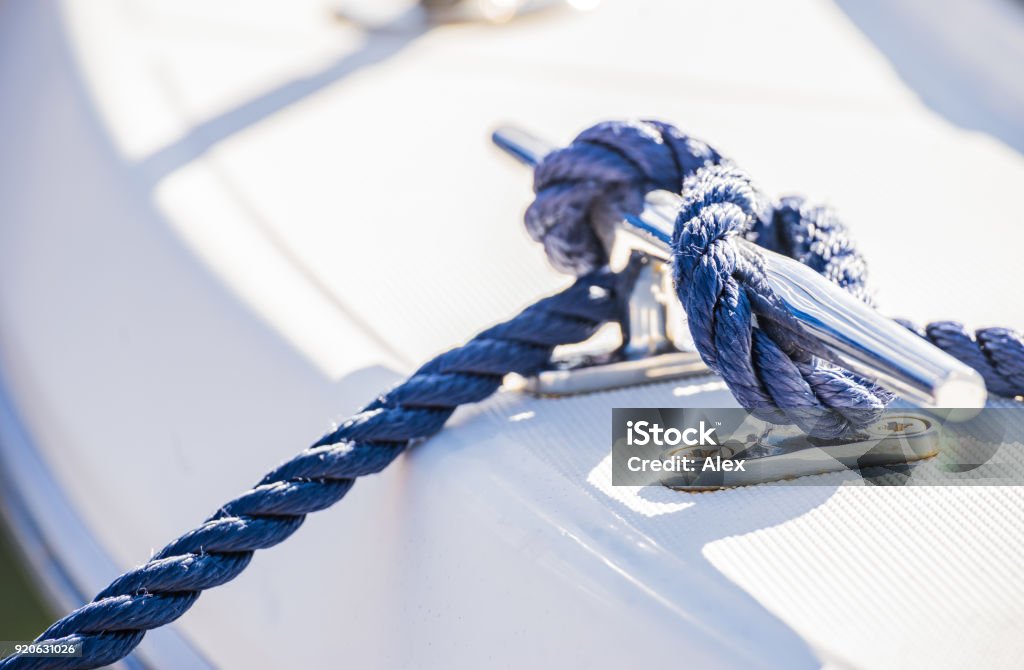 Blue nautical rope is knotted on boat cleat Detail view of blue nautical rope cleat on boat deck Mooring Line Stock Photo