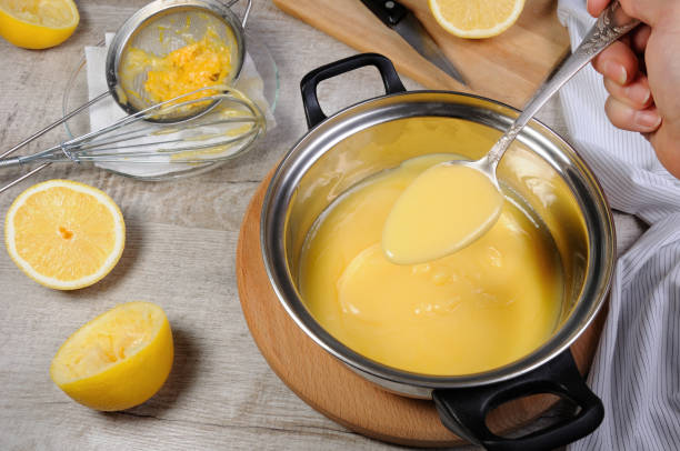 frisch zubereitete zitrone kurd - pudding auf fruchtsaft, in einem topf unter rühren mit einem löffel - zitronensaft stock-fotos und bilder