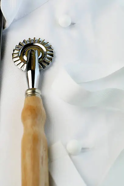 tall macro view of a chef's uniform with pastry wheel cutter. Suitable for training, apprenticeship, learning, hospitality industry.