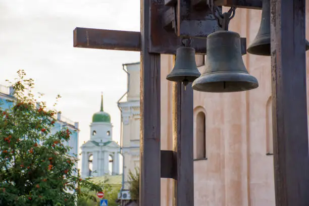 Steel bells in the foreground with the church with a green dome and rowanberry or wild ash with red fruits in the background. Evening photo on the background of the cloudy sunset sky