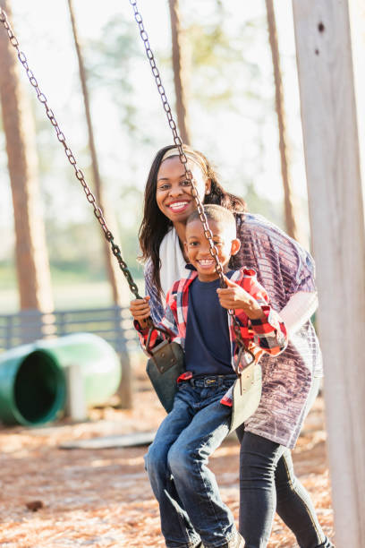 african-american chłopiec z matką na placu zabaw na huśtawce - child swinging playground african descent zdjęcia i obrazy z banku zdjęć