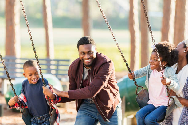 rodzina bawi się razem w parku, na huśtawkach - child swinging playground african descent zdjęcia i obrazy z banku zdjęć