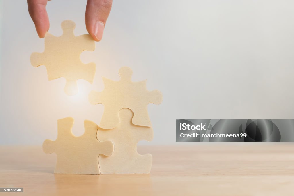 Hand of male or female putting jigsaw puzzle connecting on woodden desk, Strategic management and business solutions for success Skill Stock Photo