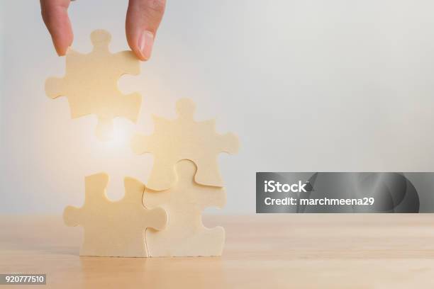 Hand Of Male Or Female Putting Jigsaw Puzzle Connecting On Woodden Desk Strategic Management And Business Solutions For Success Stock Photo - Download Image Now