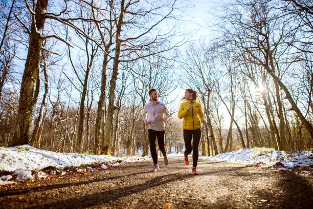 Photo of Young sporty happy couple jogging in sportswear through the forest in the sunny winter morning.