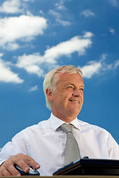 Blue Sky Thinking Business concept shot showing an older male executive using a computer with a blue sky complete with fluffy white clouds. Shot on location not in a studio. environment computer cloud leadership stock pictures, royalty-free photos & images