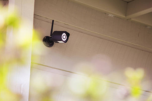 屋外防犯カメラ ヘッジの前景で家の壁にねじで締まる - screwed ストックフォトと画像
