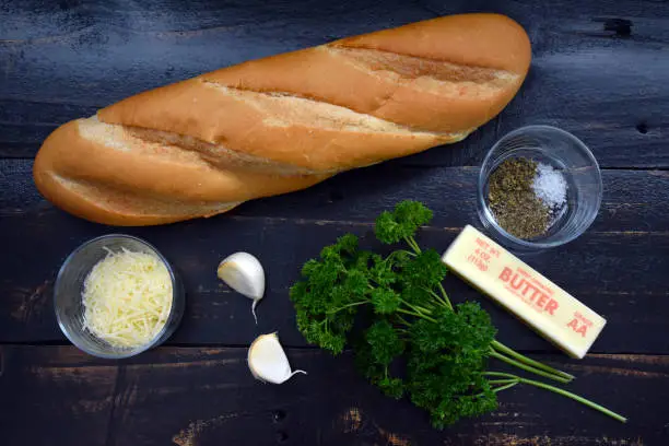 A baguette, herbs, butter, parsley, garlic cloves, and shredded parmesan cheese