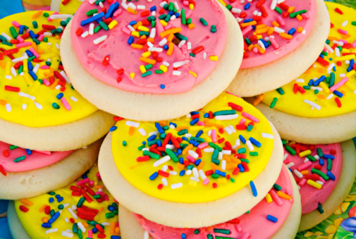 Homemade sugar cookies with a circular shape topped off with yellow and pink icing. Assorted color sprinkles are on the top of each cookie. This is a close up macro studio shot. Multi use colors can be used for Easter or springtime baking. 