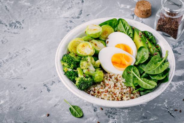Healthy green vegetarian buddha bowl lunch with eggs, quinoa, spinach, avocado, grilled brussels sprouts and broccoli with flax seeds
