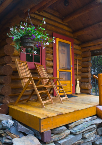 Close up shot of log cabin front porch, two wooden chairs and hanging flower basket.