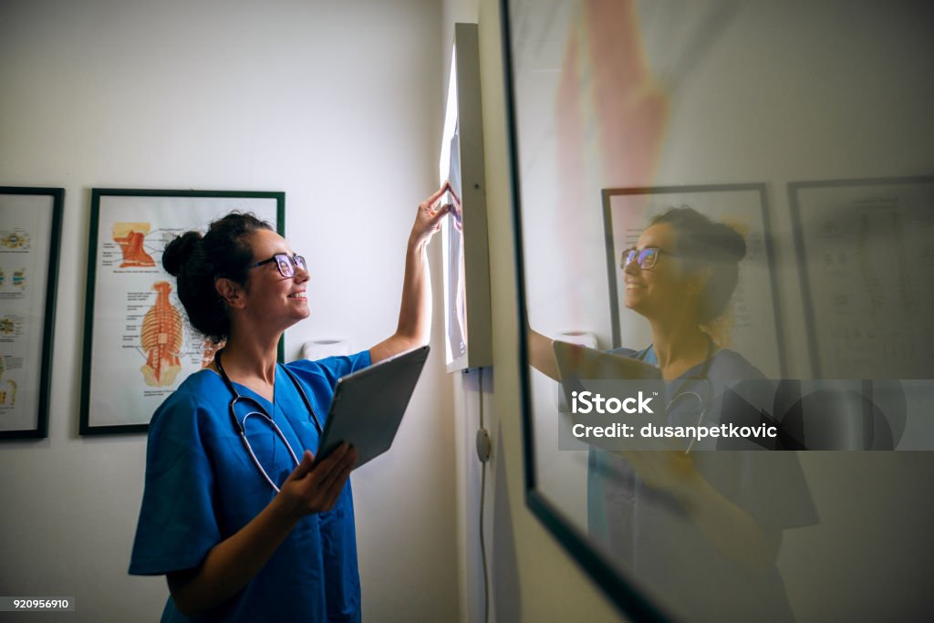 Vista laterale dell'infermiera sorridente di mezza età che controlla le radiografie in uno ufficio medico. - Foto stock royalty-free di Macchina per radiografie