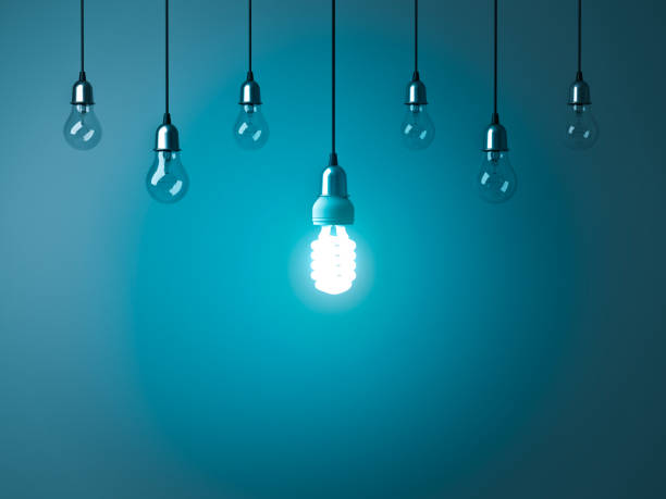 istock One hanging energy saving light bulb glowing stand out from unlit incandescent bulbs with reflection on dark cyan background 920957228