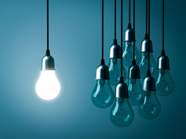 istock One hanging light bulb glowing and standing out from unlit incandescent bulbs on dark green pastel color background 920957246