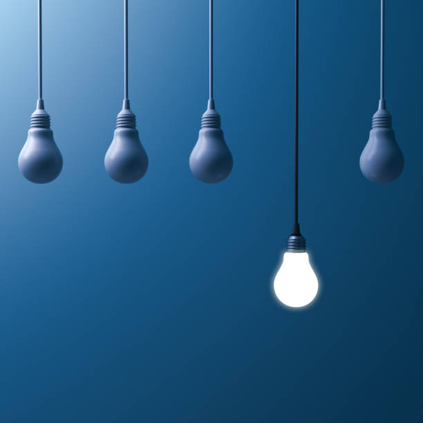 istock One hanging light bulb glowing and standing out from unlit incandescent bulbs on dark blue background 920957288