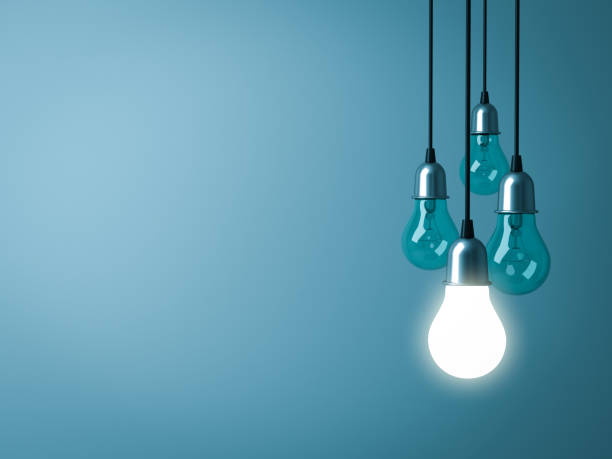 istock One hanging light bulb glowing with unlit incandescent bulbs on dark green pastel color background 920957292