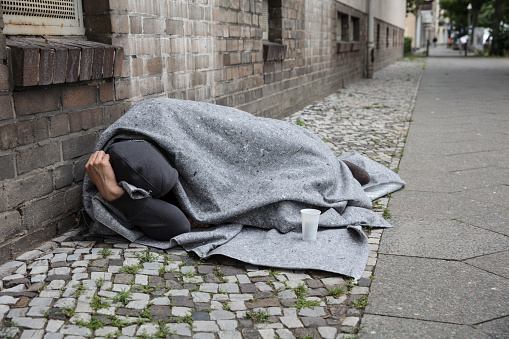 Homeless Man Covered With Blanket Sleeping On Street In City