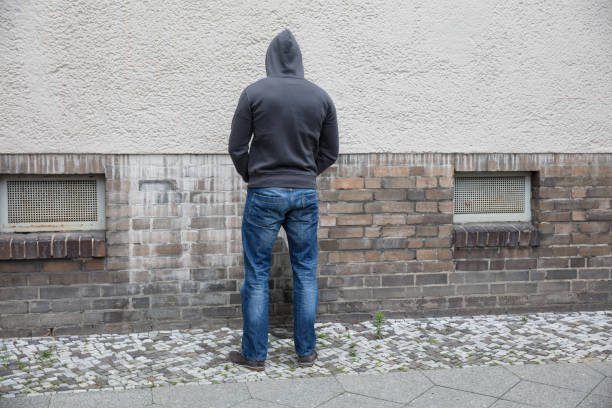 Man In Hood Peeing On Wall Rear View Of A Man In Hood Peeing On Wall In Street urinating stock pictures, royalty-free photos & images