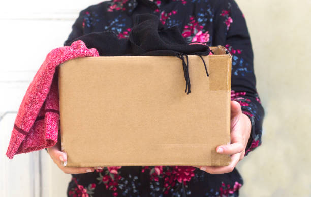 woman holding cardboard box with clothing during clothing drive - coat imagens e fotografias de stock