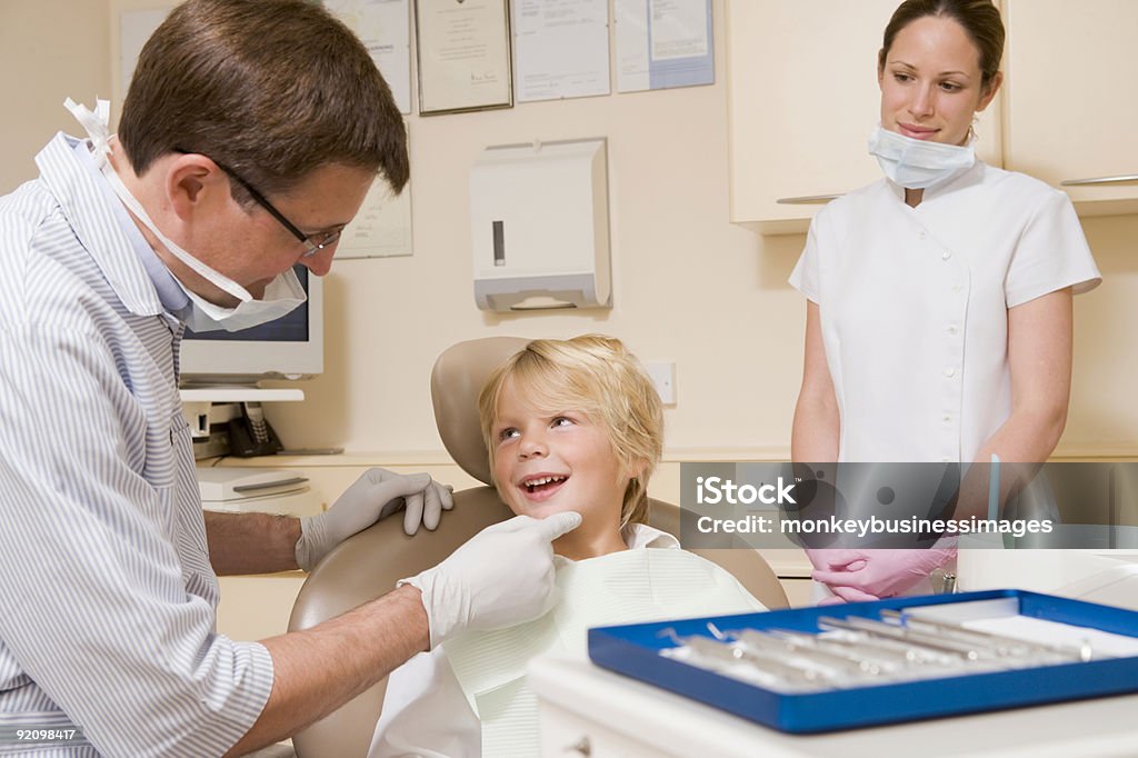 Young boy examined by a dentist while assistant looks on Dentist and assistant in exam room with young boy in chair 40-49 Years Stock Photo