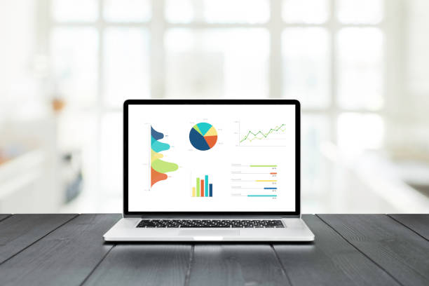 Laptop on a wooden table showing charts and graph against white office room and windows background, Analysis Business Accounting, Statistics Concept.