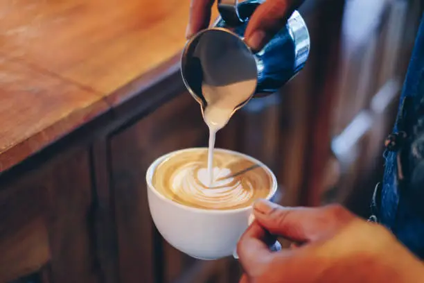 Photo of Hand barista pouring milk on coffee latte flower shape in cup