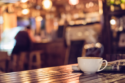 Hot espresso coffee cup with newspaper on wooden table lighting bokeh blur background