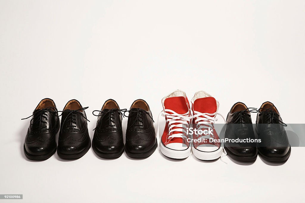 Pair of red sneakers in a row of black dress shoes  Standing Out From The Crowd Stock Photo