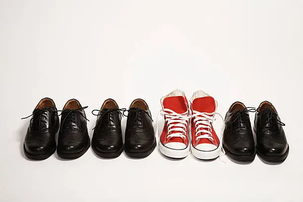 Photo of Pair of red sneakers in a row of black dress shoes