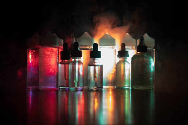 istock Vape concept. Smoke clouds and vape liquid bottles on dark background. Light effects 921012902