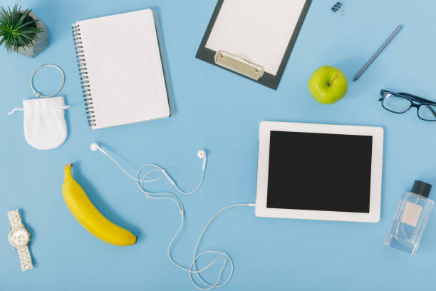 istock Flat lay, top view feminine office workspace concept. White tablet, notebook, spectacles, fruit, clipboard, pencil, perfumes, bracelet, watches and headphones 921013242