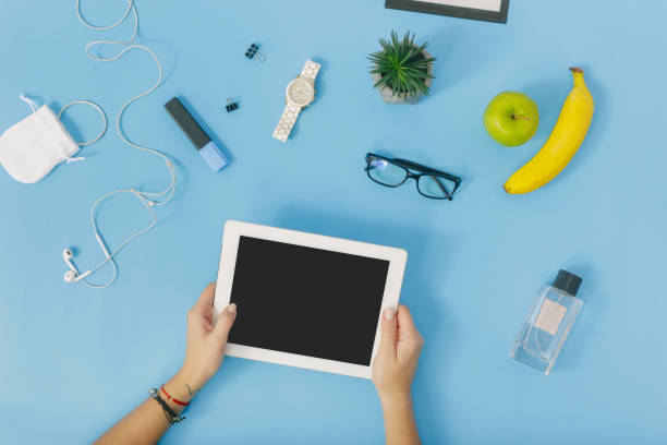istock Feminine workspace concept. Female hand holding white tablet on blue background. Flat lay, top view 921013280