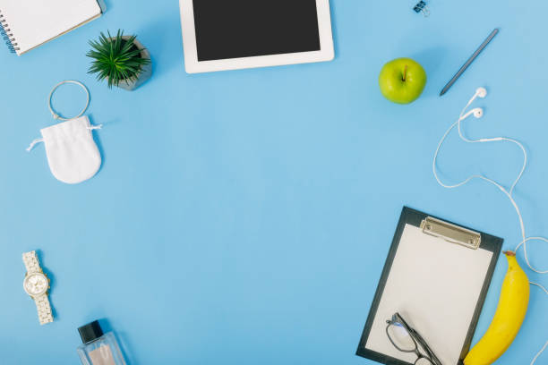 istock Frame from tablet, notebook, perfumes, spectacles, fruit, clipboard, headphones, wristwatch and pen on blue background. Feminine Workplace concept. Flat lay, top view 921013332