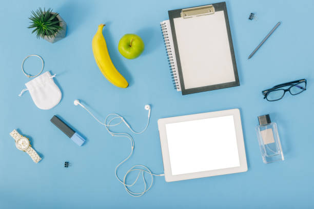 istock Feminine office workspace concept. White tablet, notebook, spectacles, fruit, clipboard, pencil, perfumes, bracelet, felt-tip pen, watches and headphones. Flat lay, top view 921013348