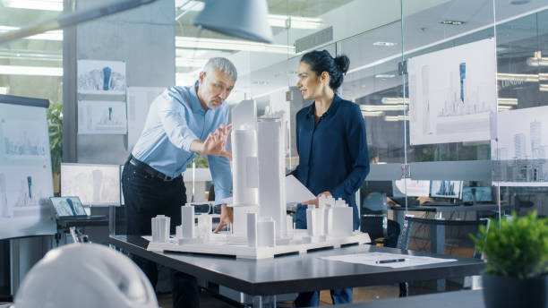 istock Chief Male Architect and Female Engineer Work with City Buildings Model. Bright People Work as Urban Planners. 921019574