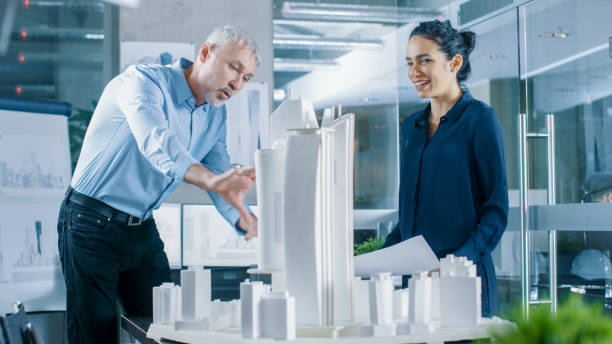 istock Two Professional Male and Female Architectural Engineers Work with Blueprints and on a Building Model Design for the Urban Planning Project. 921019612