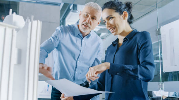 istock Two Professional Male and Female Architectural Engineers Work with Blueprints and on a Building Model Design for the Urban Planning Project. 921019622