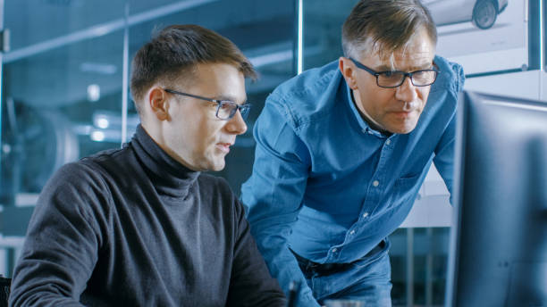 istock Experienced Senior Engineer Consults Young Designer about Project, They Have Discussion and Work on a Personal Computer. 921019678