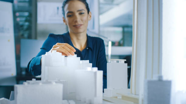 istock Female Architectural Designer Adds Component to a Building Model, She Works on a City District Urban Planning Project. Beautiful Woman in Stylish Office. 921019698