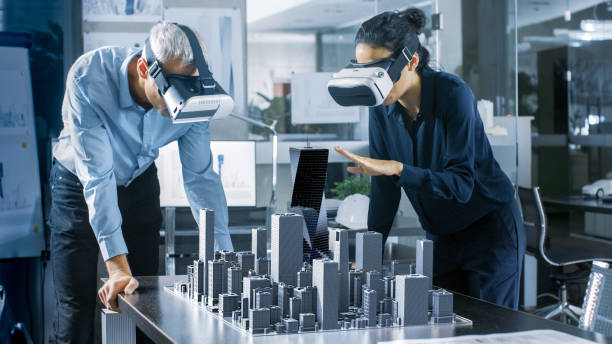 istock Male and Female Architects Wearing  Augmented Reality Headsets Work with 3D City Model. High Tech Office Professional People Use Virtual Reality Modeling Software Application. 921019720